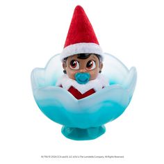 a toy with a santa hat on sitting in a blue flower bowl, looking at the camera