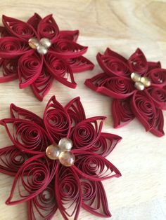 three red paper flowers with pearls on them sitting on a wooden table next to each other