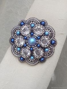 a close up of a ring on a white cloth with diamonds and blue pearls in the center