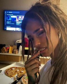 a woman with dreadlocks eating pizza in front of a tv