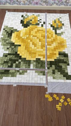 a painting made out of yellow and green tiles on the floor next to a vase with flowers