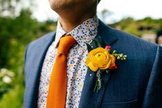 a man in a suit and orange tie with a flower pinned to his lapel