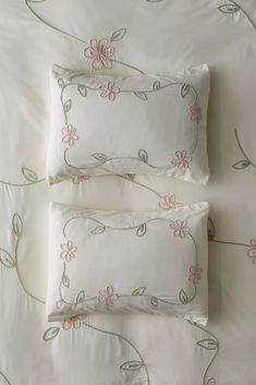 two pillows on top of a bed with white sheets and pink flowered trimmings