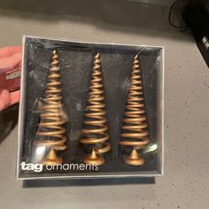 a person is holding a box with three christmas trees in it and there are gold colored spirals on the sides