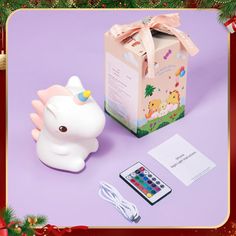 a small toy unicorn next to a box and remote control on a purple background with christmas decorations