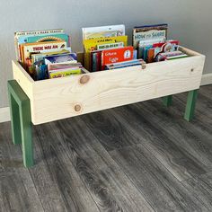 a wooden toy box with books in it on the floor next to a gray wall