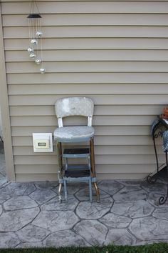 an old chair sitting in front of a house next to a small table and lamp