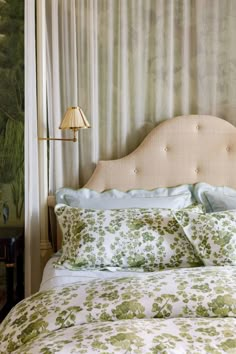 a bed with green and white floral comforter next to a lamp on a table