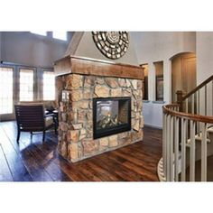 a living room with a stone fireplace and wooden floors in front of a spiral staircase