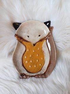 a white and brown owl brooch sitting on top of a fur covered floor with it's eyes closed