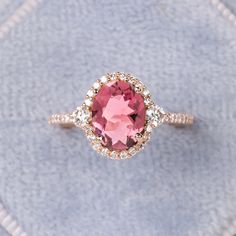 a ring with a pink stone surrounded by white and brown diamonds on a blue cloth