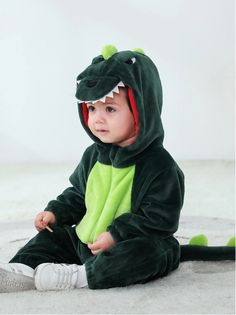 a baby in a green dragon costume sitting on the floor with his legs crossed and eyes closed