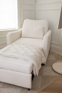 a white chair and footstool sitting in front of a window on the floor