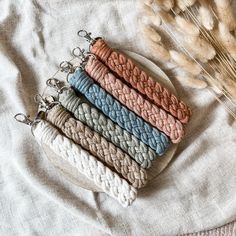 four different colored knitted key chains sitting on top of a white cloth next to some dried wheat