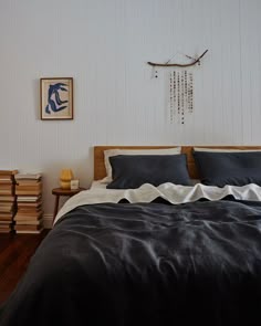 a bed with black and white sheets in a bedroom next to a wooden nightstand on top of a hard wood floor