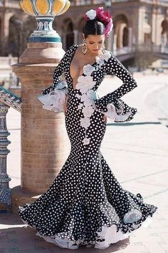 a woman in a black and white dress with polka dots on it, leaning against a pillar