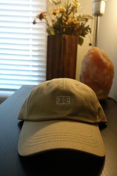 Khaki dad-hat with white, embroidered pitch over the center. Khaki Baseball Cap With Embroidered Logo And Curved Brim, Khaki Hat With Embroidered Logo And Curved Brim, Khaki Curved Brim Hat With Embroidered Logo, Casual Khaki Six-panel Dad Hat, Spring Outdoor Dad Hat Six-panel, Dad Hat With Embroidered Logo, Spring Outdoor Six-panel Dad Hat, Outdoor Dad Hat With Embroidered Logo, Six-panel, Outdoor Dad Hat With Embroidered Logo And Six-panel Shape