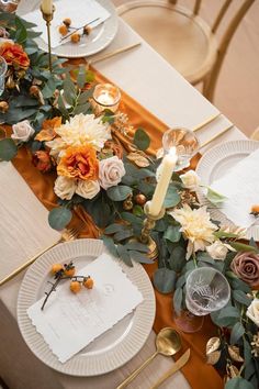 the table is set with white plates and silverware, gold napkins and flowers