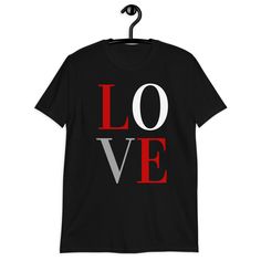 Love Sign Short Sleeve Softstyle Unisex Tee.EXCLUSIVE OF DESIGN. MADE-TO-ORDER. All you need is love. Right? Remember that sentiment every time you wear this inspirational tee. Spread love instead of hate and be the change you wish to see in the world. You will also appreciate just how soft and comfy this 100% ring-spun cotton top is. The double stitching on the neckline, sleeves and bottom hem plus shoulder-to-shoulder taping add more durability and help to ensure you keep this top for a very l Black Slogan T-shirt For Valentine's Day, Valentine's Day Black T-shirt With Text Print, Valentine's Day Black Slogan T-shirt, Valentine's Day Black T-shirt With Slogan, Black Short Sleeve T-shirt For Valentine's Day, Black T-shirt With Heart Graphic For Valentine's Day, Black Graphic Tee For Valentine's Day, Black Graphic Print Top For Valentine's Day, Charitable Giving