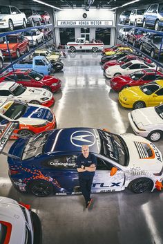 a man sitting on top of a car in a garage filled with lots of cars