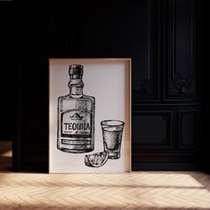 a bottle and glass sitting on top of a wooden floor next to a framed poster