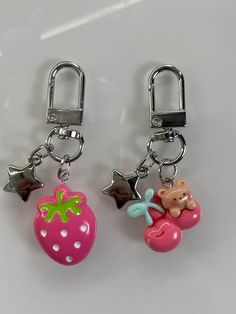 two key chains with charms attached to them on a white surface, one has a bear and strawberry