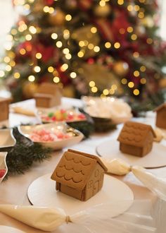 gingerbread houses are displayed on plates in front of a christmas tree