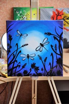 an easel with a painting on it that has dragonflies flying over the grass