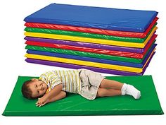 a young child laying on top of a mat next to stacks of colored mats and sheets