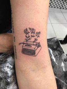 a black and white tattoo of a typewriter with flowers on it's arm