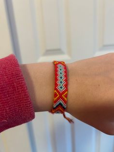 a woman's arm wearing a red bracelet with an orange and blue beaded design