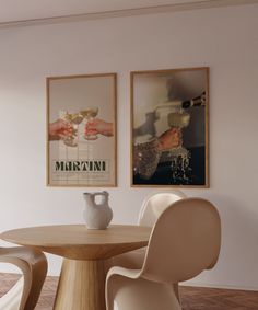 two framed pictures hang on the wall above a round table with chairs and a vase