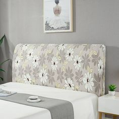 a bed with white and gray flowers on it next to a potted green plant