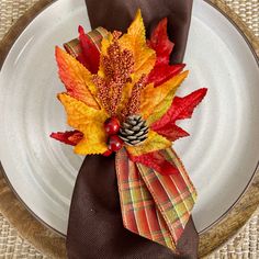 a white plate topped with a fall leaf napkin holder and a pine cone on top of it