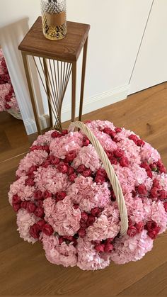 a basket filled with pink flowers sitting on top of a wooden floor next to a table