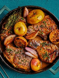 a pan filled with meat and potatoes on top of a blue table next to utensils