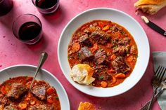 two bowls of stew and bread on a pink tablecloth next to glasses of wine