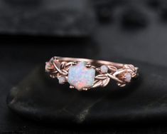 a white opal ring sitting on top of a leafy black stone slab with leaves around it