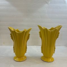 two yellow vases sitting next to each other on a white tableclothed surface