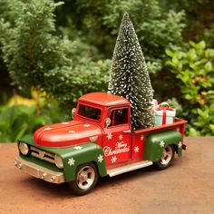 an old red truck with a christmas tree on the back is parked in front of some trees