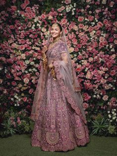 a woman in a pink lehenga standing next to a floral wall with roses