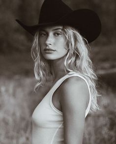 black and white photograph of a woman wearing a cowboy hat with long blonde hair standing in a field