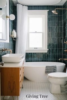 a white toilet sitting next to a bath tub under a window in a green tiled bathroom