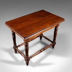 an old style wooden table with turned legs and wood grain on the top, sitting against a gray background