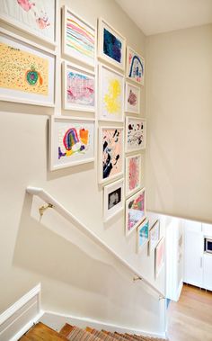 there are many framed pictures on the wall next to the stair case in this house