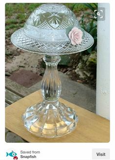 a glass cake stand with a pink flower on it sitting on a wooden table outside