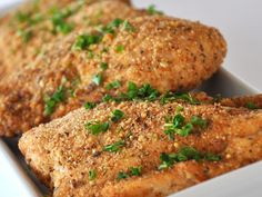 two pieces of fried chicken in a white dish with parsley on the top and green garnish