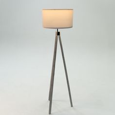 a floor lamp with a white shade on it's side and a wooden tripod base