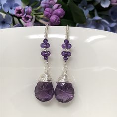 The Wisteria Path earrings weave a delicate story of rich blooms and delicate petals. These earrings feature beautiful, tender purple amethyst that have been intricately hand-carved with a unique starburst pattern and wrapped with fine sterling silver. Gracefully suspended from marquise French ear wires that are embellished with blossoms of petite, micro-faceted amethyst. Swirled, vine-like detailing on the ear wires give an extra feminine touch to these lovelies. Very lightweight, unique and oh Lavender Amethyst Earrings With Natural Stones, Elegant Purple Wire Wrapped Crystal Earrings, Purple Long Drop Earrings With Natural Stones, Lavender Amethyst Earrings With Ear Wire, Lavender Amethyst Drop Earrings, Purple Briolette Earrings With Natural Stones, Handmade Amethyst Crystal Earrings, Purple Briolette Wire Wrapped Earrings, Handmade Elegant Amethyst Crystal Earrings