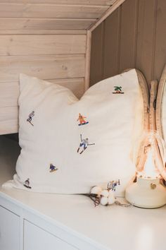 a white pillow sitting on top of a white dresser next to a clock and lamp